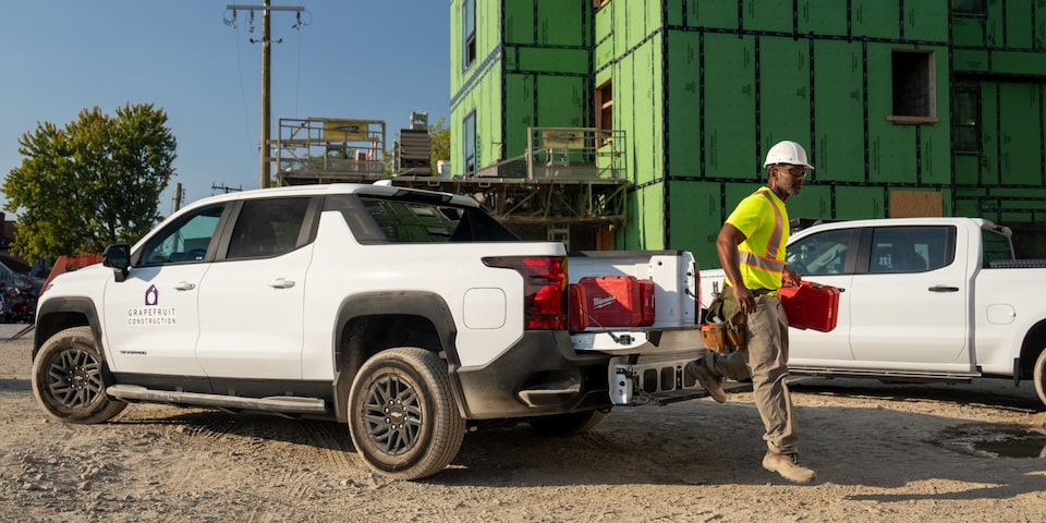 A construction worker carries tools from the back of a Chevrolet SIlverado EV tailgate.
