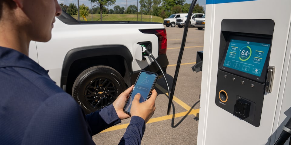 A driver is charging their Silverado EV at a charging station and checking the status from their phone.
