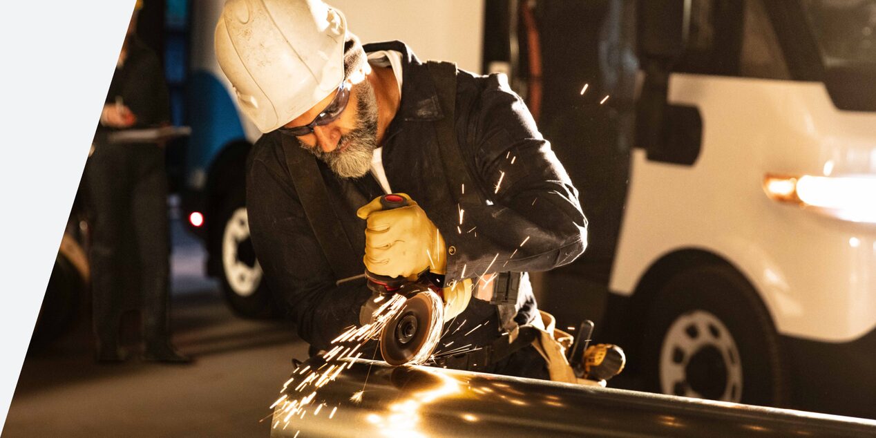 A man in a hardhat using a grinder in a shop with a Brightdrop in the background.