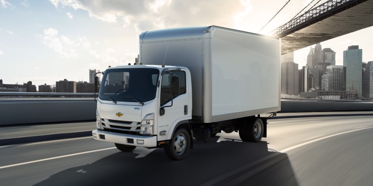 A Chevrolet truck with a cargo body upfit applciation driving on the highway.