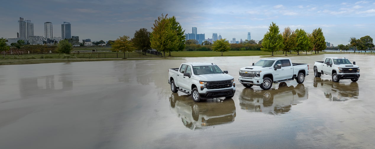Three white Chevrolet Silverados parked in a large wet parking lot. 