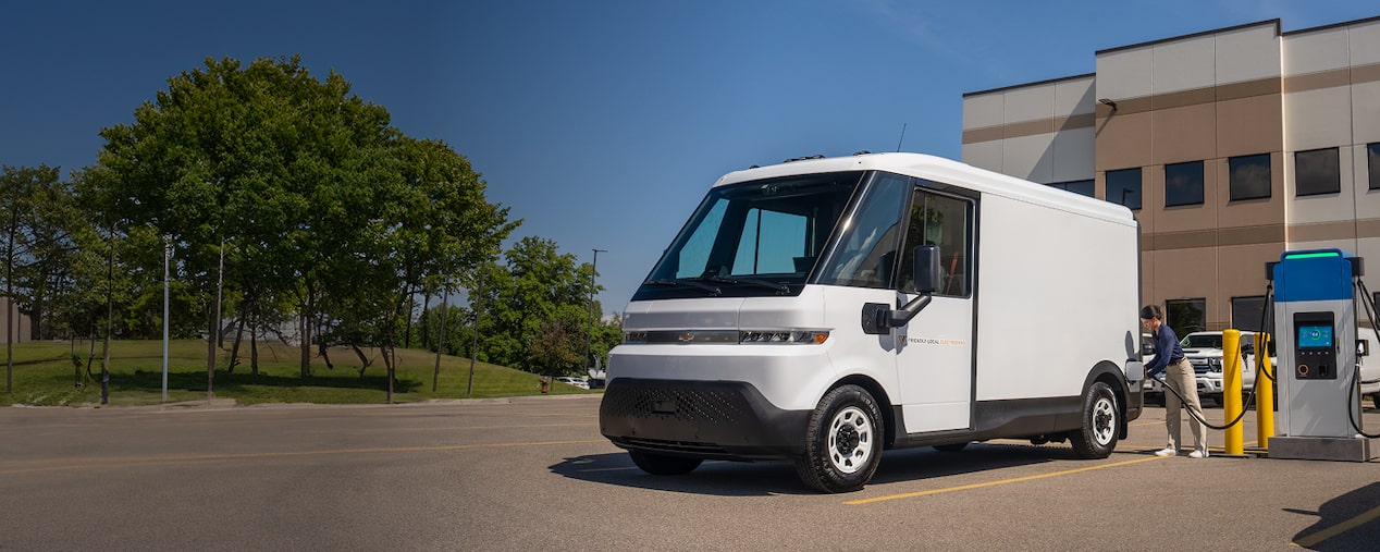 A white Chevrolet BrightDrop getting plugged in at an EV charging station