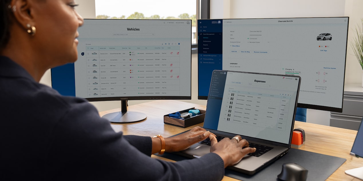 Vehicle telematics being viewed on a laptop and two monitors by an office worker.