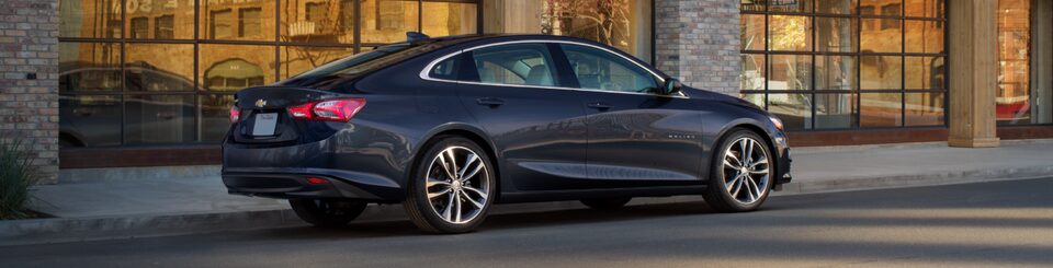 Rear Three-Quarters View of the 2024 Chevrolet Malibu Parked In Front of a Building
