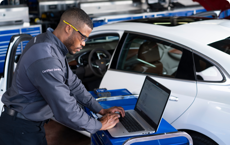 A GM Technician Working on a Laptop Standing Next to a Vehicle