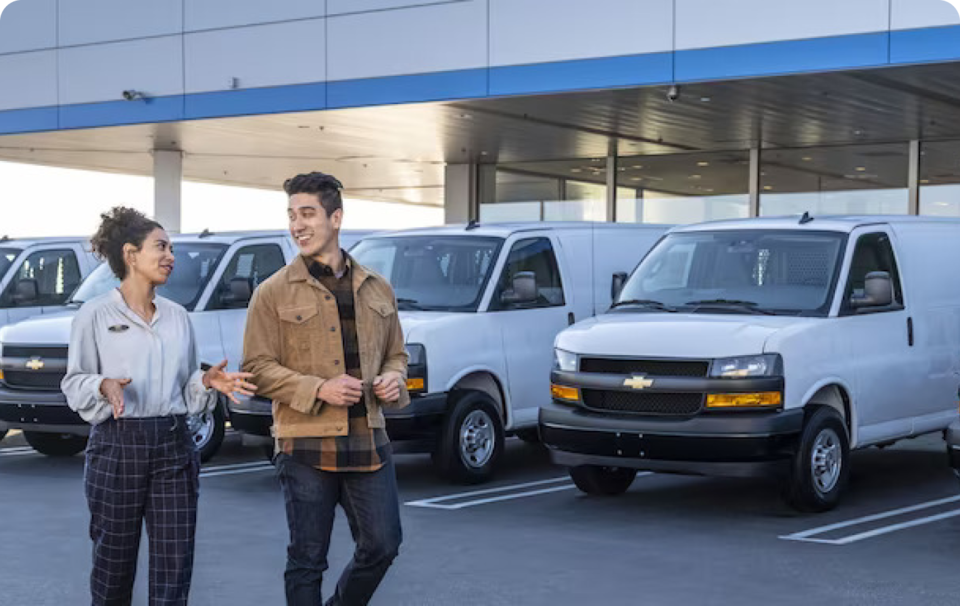 A Man and a Woman Walking Together Talking with Chevrolet Vans in the Background